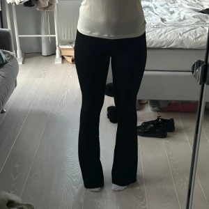 Svarta byxor från Gina Tricot - Snygga svarta byxor från Gina Tricot med en tight passform upptill och utsvängda ben. Perfekta för en stilren look. Byxorna är tillverkade i ett mjukt och stretchigt material för extra komfort. Storlek S och den långa modellen för Tall. Jag står på tå i bilderna då de är för långa för mig. Passar nog någon som är runt 173-178 bra