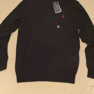 Navy tröja från Polo Ralph Lauren - Säljer en stilren navy tröja från Polo Ralph Lauren med rund hals och det klassiska röda logotypen på bröstet. Tröjan är tillverkad i bomull och har långa ärmar. Perfekt för en avslappnad och snygg look.
