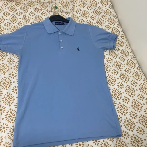 Ljusblå pikétröja från Ralph Lauren - Säljer en stilren ljusblå pikétröja från Ralph Lauren. Tröjan har en klassisk krage och tre knappar framtill. Den ikoniska loggan är broderad på bröstet. Perfekt för en avslappnad men ändå snygg look. Har använd den 2 ggr. Denna storleken är L fast det passar också till personer som har M i storlek. Kontakta mig DM för fler frågor om tröjan!