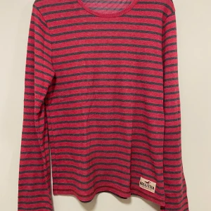 Röd och svart randig tröja från Hollister - Säljer en snygg röd och svart randig tröja från Hollister. Tröjan har långa ärmar och en rund halsringning. Perfekt för en avslappnad stil. Hollister-loggan är synlig längst ner på tröjan. Sparsamt använd, så fint skick. Passar strl S/M.