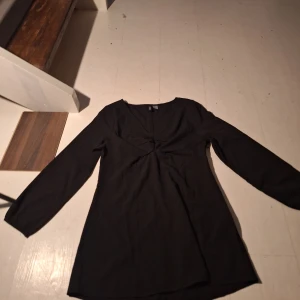 Svart klänning med v-ringning - Elegant svart klänning med v-ringad hals och långa ärmar. Perfekt för en stilren look. Klänningen har en enkel design som gör den lätt att matcha med olika accessoarer.