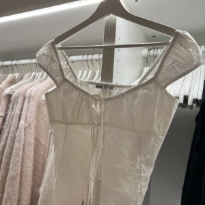 Vit topp från Bershka - Säljer en stilren vit topp från Bershka med knytning framtill. Toppen har korta ärmar och en smickrande passform. Perfekt för att skapa en chic look.