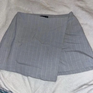 Grå omlottkjol med ränder - Snygg grå omlottkjol med subtila ränder. Perfekt för en stilren look. Kjolen har en klassisk omlottdesign som ger en elegant touch.