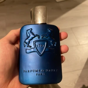Parfym Parfums de Marly Layton - Säljer en flaska Parfums de Marly Layton, en lyxig herrparfym i en elegant blå flaska med silverdetaljer. Flaskan har en stilren design med två upphöjda hästar och texten '1743'. Kommer i en snygg förpackning med svart och silverrandigt mönster. Korken sitter inte bra, den sitter inte fast, skicka innan köp