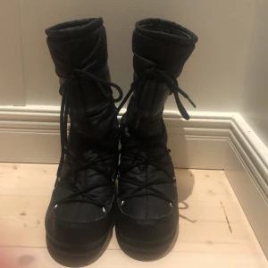 Svarta Moon Boots - Säljer ett par svarta Moon Boots i storlek 38. De är vattentäta och har snörning för en säker passform. Perfekta för kalla vinterdagar med sin robusta design och varma foder.