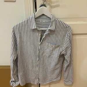 Randig skjorta från Zara - Säljer en stilren randig skjorta från Zara i blått och vitt. Skjortan har långa ärmar och knappar framtill samt en bröstficka. Perfekt för en avslappnad men ändå snygg look.