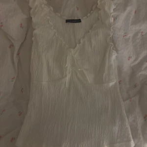 Vit topp med volangdetaljer - Säljer en söt vit topp med volangdetaljer och knyt framtill. Från brandy använd ca 2 gånger dvs mycket fint skick!