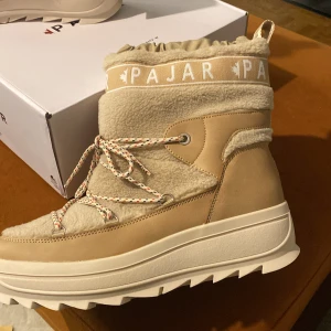 Beige vinterboots från Pajar - Snygga och varma beige vinterboots från Pajar med snörning och vadderad insida. Skorna har en robust sula och är perfekta för kalla dagar. De har en kombination av syntet och fleece för extra komfort och stil. Nya och i original förpackning 