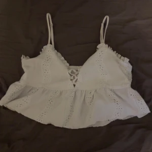 Vit spetsprydd linne topp - Söt vit linne topp med spetsdetaljer och smala axelband. Toppen har en volangkant och snörning framtill. Perfekt för sommaren!💕