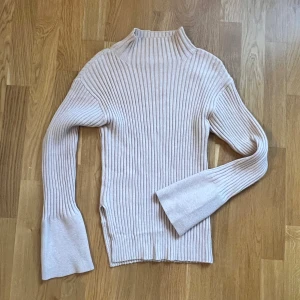 Beige ribbad polotröja - Säljer en stilren beige ribbad polotröja med långa ärmar. Perfekt för kyligare dagar och ger en elegant look. Tröjan har en hög krage och är tillverkad i ett mjukt material som känns skönt mot huden. Tröjan har en slits på sidan.