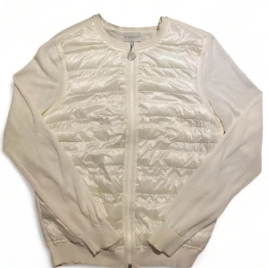 Beige jacka från Moncler - Säljer en stilren beige jacka från Moncler med quiltad design och dragkedja framtill. Jackan har långa ärmar och en rund halsringning. Perfekt för en elegant look.