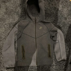  mörk blå nike tech fleece från Nike  - Säljer en mörk blå hoodie från Nike med dragkedja och luva. Hoodien har två praktiska fickor med dragkedjor framtill och en diskret Nike-logga på bröstet. Perfekt för en avslappnad stil,använd i en månad sedan passar till någon som är  150-160 pris 600kr. Pris kan diskuteras med snabb affär 