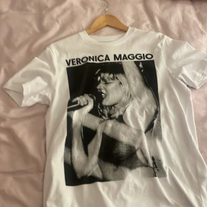 Vit t-shirt med Veronica Maggio-tryck - Snygg vit t-shirt med ett stort svartvitt tryck av Veronica Maggio på framsidan. Perfekt för fans av artisten! T-shirten har en klassisk rund hals och korta ärmar.