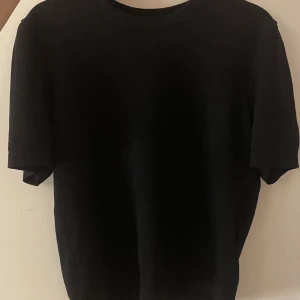 Svart stickad t-Shirt från H&M Divided  - Säljer en stilren svart tröja från H&M Divided. Tröjan har korta ärmar och är stickad i tunnt material!😊🫶🏻 För mer bilder skriv till mig. Använd 2 gånger och säljs för att den är för kort för mig!