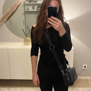 Svart axelväska från Valentino - Snygg svart axelväska från Valentino med justerbar axelrem och dragkedja. Väskan har en stilren design med logotypen präglad på framsidan och en ficka på baksidan. Perfekt för att bära dina nödvändiga saker.