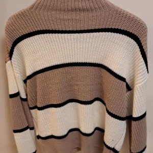 Randig stickad tröja med polokrage - Mysig stickad tröja med breda ränder i beige, vit och svart. Tröjan har en hög polokrage och långa ärmar. Köpt för 1 år sen säljer den för gillar inte färgerna är fortfarande i jättebra skick!