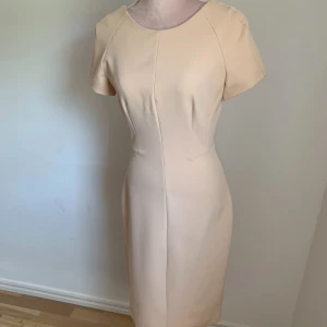 Beige klänning - Elegant beige klänning med korta ärmar och figurnära passform. Perfekt för en stilren look.