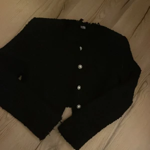 Svart kavaj med knappar - Snygg svart kavaj med dekorativa knappar framtill. Perfekt för en stilren look. Kavajen har en klassisk design med långa ärmar och en elegant passform. Aldrig använt