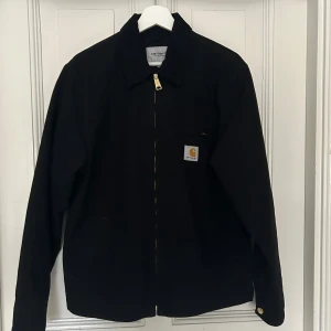 Svart Detroit Jacka från Carhartt - Säljer en svart Detroit jacka från Carhartt i storlek M. Tillverkad av 100% certifierad ekologisk bomull, perfekt för en stilren look. Jackan är enbart använd ett fåtal gånger! 