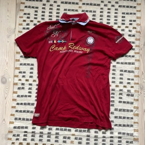 Drainer piké  - Snygg röd pikétröja från Camp Redway med broderade detaljer och flaggor. Tröjan har korta ärmar och en klassisk krage med knappslå. Perfekt för en avslappnad stil med en touch av maritimt tema.