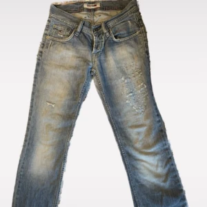 Snygga tommy hilfigher jeans - Snygga blå lågmidjade jeans från Tommy Hilfigher med slitna detaljer! De är straight leg skulle jag säga där de sitter tajt vid låren men lösare vid smalbenen och så! Innerben är 83 cm och midjemått är 70 cm. Väldigt snygg färg och designen på låren och bakfickan är super snyggt! 