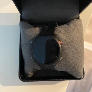 Svart Garmin smartwatch - Säljer en stilren svart Garmin smartwatch med rund urtavla och flera funktioner. Klockan har en svart rem och är perfekt för den teknikintresserade. Den är designad för att passa både till vardag och träning. Har ingen laddare till den 