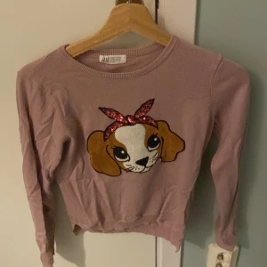 Rosa tröja med hundmotiv från H&M - Säljer en söt rosa tröja från H&M med ett stort hundmotiv på framsidan. Tröjan har långa ärmar och en rund halsringning. Perfekt för den som älskar djurmotiv! 🐶