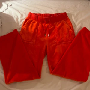Orange mjukisbyxor från Juicy Couture - Snygga orange mjukisbyxor från Juicy Couture med snörning i midjan och praktiska fickor både fram och bak. Dessa byxor är dock uppsydda. På insidan av ett ben är 67cm. Köpte dem för ca 600kr