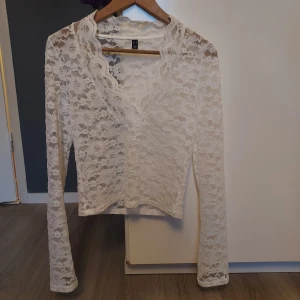 Vit spetsblus - Säljer en elegant vit spetsblus med långa ärmar och v-ringad design. Perfekt för en stilren look. Blusen är i ett mjukt och bekvämt material som ger en feminin touch.