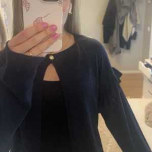 Svart kofta med volangdetaljer - Snygg marinblå kofta med volangdetaljer på axlarna och en guldknapp(originellt kommer den med en stjärnknapp, men den skickas med ifalll man vill sy dit den istället).⭐️ Perfekt för att ge en stilren touch till din outfit, passar till alla tillfällen!