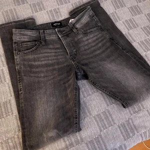 Gråa slim fit jeans Jack And Jones - Snygga grå jeans från Jack & Jones, modell Slim/Glenn. De har en slim passform och är tillverkade i ett bekvämt denimtyg. Perfekta för en stilren look med klassiska fem fickor och knappgylf. Sitter väldigt bra och passar till allt!