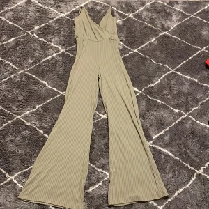 Beige ribbad jumpsuit från Bik Bok - Snygg beige ribbad jumpsuit från Bik Bok i storlek XS. Den har en omlott-design med smala axelband och vida ben. Perfekt för en stilren look!