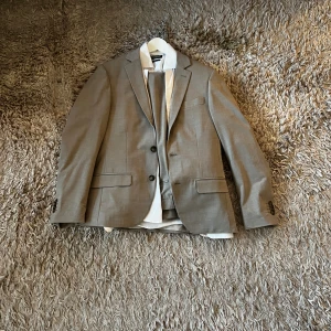 Beige Dressmann kostym - Snygg beige kostym från Dressmann med klassisk passform. Kavajen är i storlek 46S och kostymbyxorna är i storlek 31/32. Vit skjorta från dressman ingår också, slim fit. Säljs då den inte passar längre. Använd enbart 1 gång. Skriv vid frågor! 🕴🏼