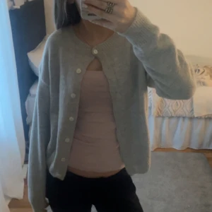 Beige kofta med knappar - Mysig grå kofta med knappar framtill. Perfekt för kyligare dagar och lätt att matcha med olika outfits. Koftan har en avslappnad passform och långa ärmar.