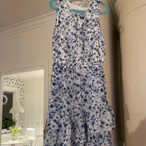 Blommig klänning från Hampton Republic - Säljer en söt blommig klänning från Hampton Republic i storlek 146. Klänningen är ärmlös med ett vackert blått blommönster på vit bakgrund. Den har volanger som ger en fin detalj och rörelse. Perfekt för somriga dagar! 🌸