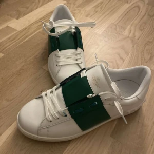 Valentino sneakers med gröna detaljer - Snygga vita sneakers från Valentino med gröna detaljer. Skorna har en stilren design med snörning och är perfekta för en trendig look.