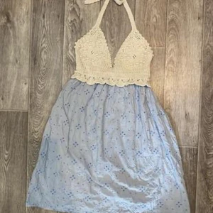Söt babydoll klänning med virkad topp - Charmig klänning med en virkad beige topp och ljusblå kjol med små blommor. Den har en halterneck-design och är perfekt för varma dagar. Kjolen är luftig och ger en avslappnad känsla.