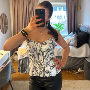 Vit korsettopp med svart mönster från Pretty Little Thing - Snygg vit korsettopp med abstrakt svart mönster. Axelbandslös design som ger en elegant look. Perfekt för att lyfta vilken outfit som helst. Aldrig använd och lappen sitter kvar! 