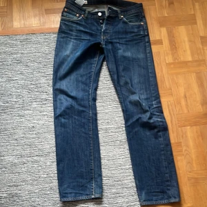 Levi's 501 jeans - Klassiska Levi's 501 jeans i blå denim. De har en rak passform och knappar i gylfen. Perfekta för en avslappnad stil med en tidlös design. Slitage vid rumpan kan lagas.