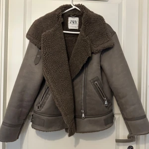 Jacka från Zara - Snygg och trendig jacka i en mörkgrå/brun nyans. Jackan har en avslappnad passform med en asymmetrisk dragkedja framtill. Den har en varm teddyfoder i kragen och är perfekt för kallare väder. Jackan har fickor med dragkedjor och detaljer i konstläder. En stilren och tidlös jacka som passar till många olika outfits. Har använts en gång och är i mycket bra skick💕