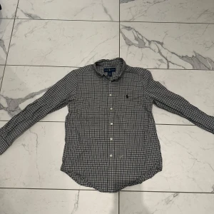 Rutig skjorta från Ralph Lauren - Säljer denna snygga blå rutig skjorta från Ralph Lauren med klassisk krage och knappar framtill. Skjortan är i skick 8/10 och i  storlek 10-12 år! Orginal pris - 1100kr Vårat pris - 149kr. Priset är inte hugget i sten! Skriv vid minsta lilla fundering!🙌