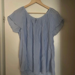 Ljusblå blus Kappahl  - Säljer en luftig och bekväm ljusblå blus med korta ärmar. Perfekt för varmare dagar med sin avslappnade passform och mjuka material. Blusen har en enkel design med en liten knappdetalj vid halsen.