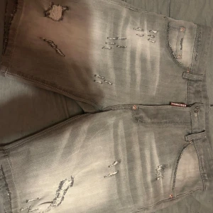 Grå jeansshorts från DSQUARED2 - Säljer ett par grå jeansshorts från DSQUARED2 med slitna detaljer och en cool, avslappnad look. Shortsen har en klassisk femficksdesign och knappgylf. Perfekta för en trendig stil! Oanvända pga de ej passa mvh 