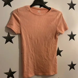 Rosa ribbad t-shirt från FSB Sister - Säljer en söt rosa ribbad t-shirt från FSB Sister i storlek XS. Den har en klassisk rund hals och korta ärmar, perfekt för en avslappnad stil. Passar bra till jeans eller kjol för en enkel look.