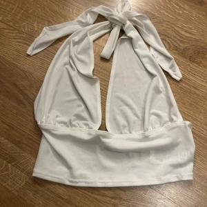 Vit halterneck topp från NLY One - Säljer en snygg vit halterneck topp från NLY One. Toppen har en öppen rygg och knytband i nacken. Perfekt för sommarens varma dagar eller en utekväll. Materialet är mjukt och stretchigt för en bekväm passform.