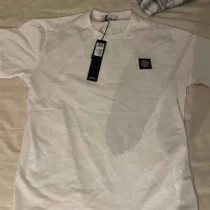 Vit t-shirt från Stone Island(Bara testad) - Säljer en stilren vit t-shirt från Stone Island med deras ikoniska logga på bröstet. T-shirten är kortärmad och tillverkad i mjukt material för en bekväm passform. Perfekt för en avslappnad look. Köpte denna vara innan på Plick men passade inte.