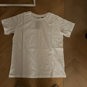 Vit t-shirt  - Säljer en klassisk vit t-shirt  i mjukt material. Perfekt basplagg med rund hals och korta ärmar. Passar till allt och är ett måste i garderoben.