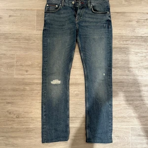 Blå jeans från Tommy Hilfiger - Snygga blå jeans från Tommy Hilfiger med en slim fit passform. De har en klassisk femficksdesign och en diskret slitning på ena benet. Perfekta för en stilren look med en touch av edge.