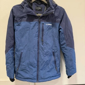 Blå vinterjacka från Everest stl 164 - Säljer en snygg blå vinterjacka från Everest i mycket bra skick. Jackan har en dragkedja framtill och praktiska fickor med dragkedjor. Den är perfekt för kalla dagar med sin varma och skyddande design. Huvan är justerbar och ger extra skydd mot väder och vind. Perfekt för vintern! ❄️