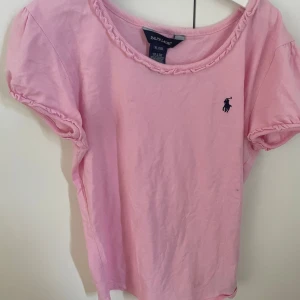 Rosa t-shirt från Ralph Lauren - Säljer en söt rosa t-shirt från Ralph Lauren i storlek L. Jag skulle säga att den passar s. Den har korta ärmar och ett litet broderat logotyp på bröstet. Perfekt för en avslappnad stil i vår och sommar. T-shirten är i bra skick och gjord av mjukt bomullsmaterial.